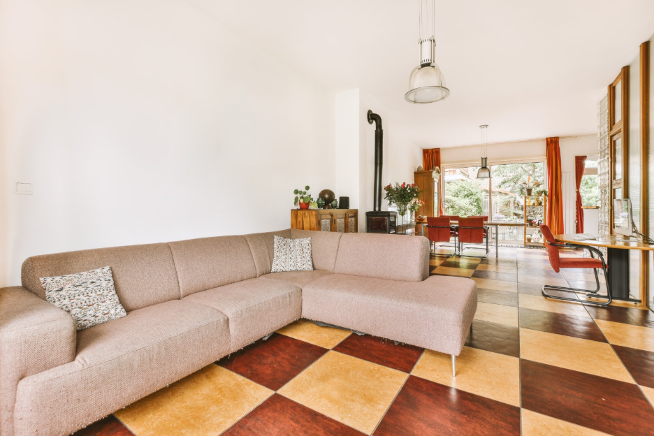 Open-plan living and dining room featuring bold geometric flooring in warm wood tones, with a large sectional sofa and dining area